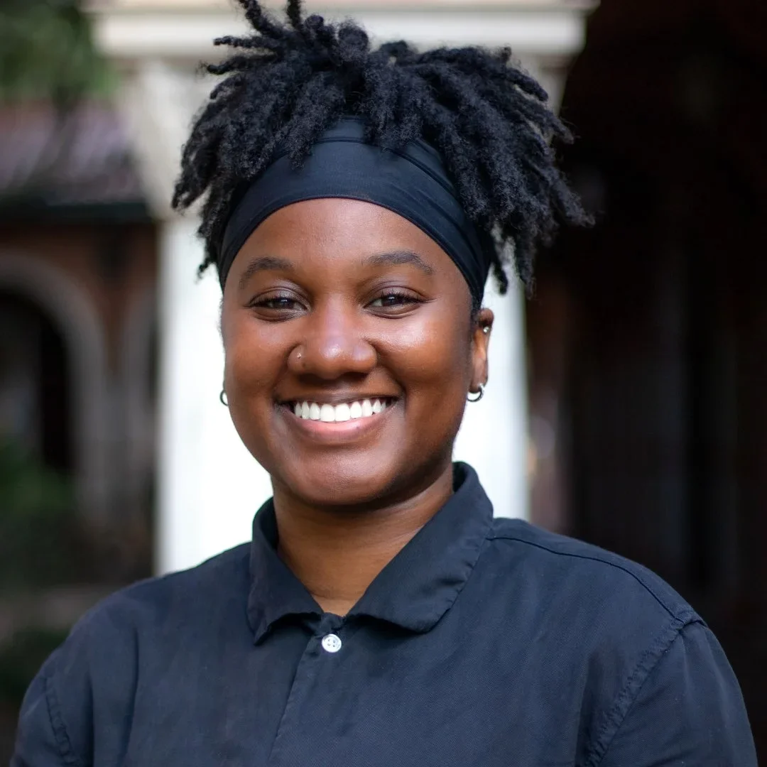 This photo pictures School of Humanities and Arts Digital Marketing Manager, Peyton Ball, smiling in a Rice University courtyard. She is wearing a black button down and her hair is up in a ponytail.