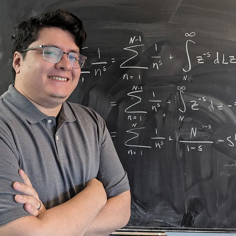 photo of Daniel Flores in front of a chalkboard with formulas